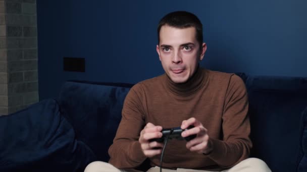 Возбужденный молодой кавказский мужчина геймер держит контроллер, играющий в видеоигры, сидя на диване, чувствуя себя вне себя счастливым в видеоигре в одиночестве дома — стоковое видео