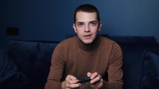 Feliz emocionado joven caucásico hombre gamer celebración controlador jugando videojuegos sentado en sofá sensación de alegría celebrando la victoria ganar en el videojuego solo en casa — Vídeo de stock