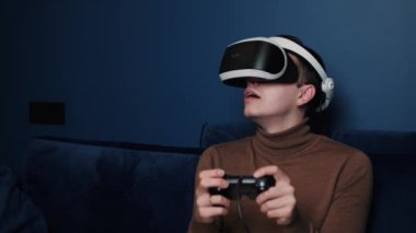 Çekici beyaz adam joystick 'i tutuyor ve evdeki koltukta sanal gerçeklik gözlüğü başlığı takıyor. Evde VR gözlük kullanarak oyun oynayan mutluluk oyuncusuName.