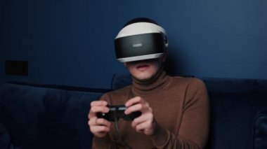 Çekici, korkmuş beyaz adam joystick 'i tutuyor ve evdeki koltukta sanal gerçeklik gözlüğü başlığı takıyor. Evde VR gözlük kullanarak oyun oynayan korkak oyuncu..