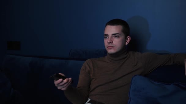Hombre joven caucásico relajarse en el sofá acogedor, la elección de la película en línea, ver programas de entretenimiento, pasar el fin de semana libre solo en el sofá en casa. — Vídeos de Stock