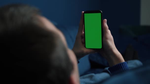 Mężczyzna leżący na kanapie za pomocą smartfona z chroma key zielony ekran w nocy, przewijanie przez media społecznościowe lub sklep internetowy - internet, koncepcja komunikacji zbliżenie. — Wideo stockowe
