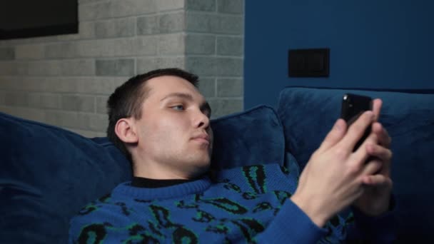 Close up Young kaukasiske Mand Bruger Smartphone mens om på en sofa i hjemmet. Mand browser gennem internettet, ser videoer og bruger sociale netværk i hjemmet. – Stock-video