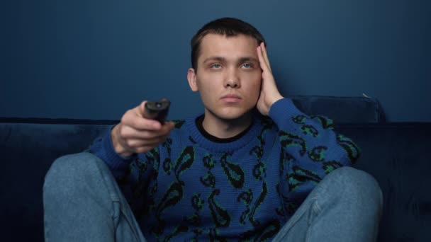 Junger kaukasischer Mann entspannt sich auf gemütlicher Couch, wählt Online-Film, schaut unterhaltsame Sendungen, verbringt freie Wochenendzeit allein auf dem Sofa zu Hause. — Stockvideo