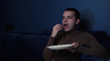 Sıkıcı ve mutsuz bir adam televizyon izliyor ve patlamış mısır fırlatıyor. Erkek, bütün gün televizyon izleyip koca bir kase patlamış mısırla kanepede oturuyor.