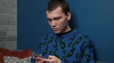 Genç, yakışıklı beyaz adam evde akıllı telefon kullanıyormuş. Man İnternet 'e Bakar, Video İzler ve Evde Sosyal Ağ Kullanır.