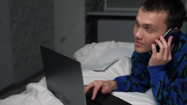 Przystojny biały mężczyzna rozmawiający przez komórkę w sypialni w domu. Portret mężczyzny relaksujący się w łóżku i rozmawiający na smartfonie — Wideo stockowe
