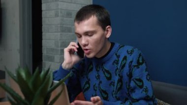 Ofiste bilgisayarla çalışırken telefonda konuşan beyaz bir adam var. Yavaş çekim.