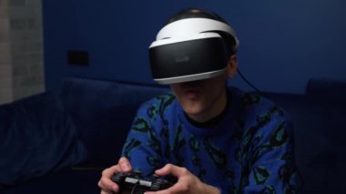 Portreyi kapat beyaz adam joystick 'i tut ve evdeki koltukta sanal gerçeklik gözlüğü kulaklığı tak. Evde VR gözlük kullanarak oyun oynayan mutluluk oyuncusuName.
