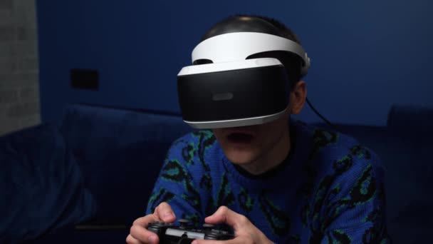 Közelkép portré Vonzó kaukázusi férfi tartsa joystick és viseljen virtuális valóság szemüveg fejhallgató sisak kanapén otthon. Boldogság játékos játék segítségével VR szemüveg otthon. — Stock videók