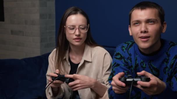 Šťastní mladí lidé hrají videohry na konzoli, zatímco sedí na gauči před televizí. Millennial pár tráví zábavný čas spolu doma. — Stock video
