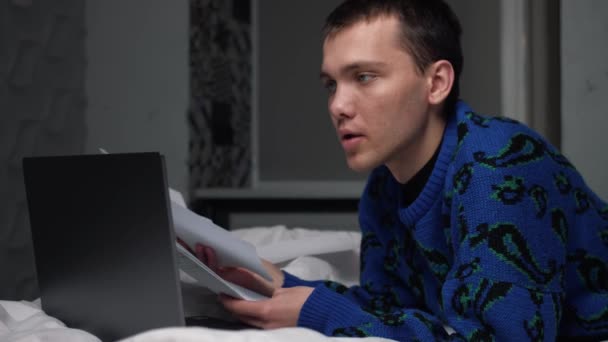 Człowiek z papierowymi dokumentami pracujący na laptopie w łóżku. Zmęczony człowiek pracujący w domu. Facet pracuje na laptopie w domu., — Wideo stockowe