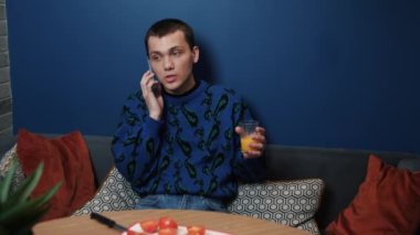 Mutfakta oturan yakışıklı beyaz adam yemek pişirmekten dikkati dağılmış ve akıllı telefondan konuşuyor. Yaşam tarzı, salata hazırlıkları sırasında hoş sohbetler