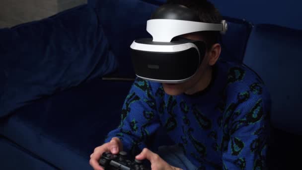 매력적으로 흥분 한 코카서스 남자는 조이스틱을 들고 집 소파에서 가상 현실 안경 헤드셋 헬멧을 착용 한다. 가정에서 VR 안경을 사용하여 게임을 하는 행복 게이머. — 비디오