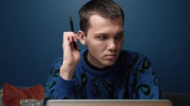 Düşünceli, ciddi, beyaz erkek öğrenci yazar. Ev ofisinin masasında dizüstü bilgisayarla oturuyor. Düşünce konseptinde kaybolmuş, ilham verici, sorunlu, çözüm fikirleri düşünüyor.