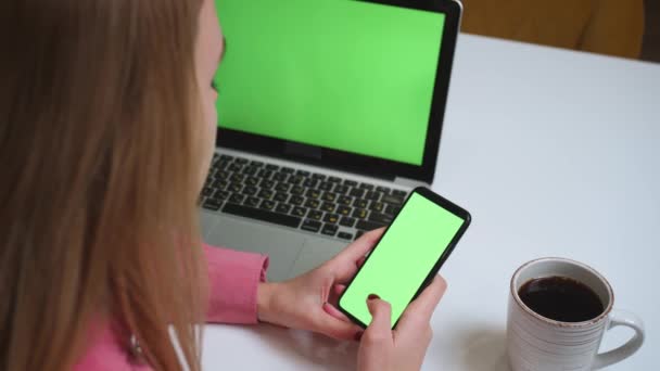 Feche a mulher usando a tela verde do smartphone na mesa com o computador portátil Chromakey. Close up tiro de mulheres mãos segurando telefone celular deslizando tela verde.. — Vídeo de Stock