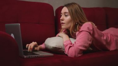 Genç ve güzel bir kadın dizüstü bilgisayar kullanıyor. Ekrana bakıyor, evdeki kanepede yatıyor. Bilgisayarda sohbet eden, internette gezen sosyal medyada okuyan ya da evde çalışan bir kadın..