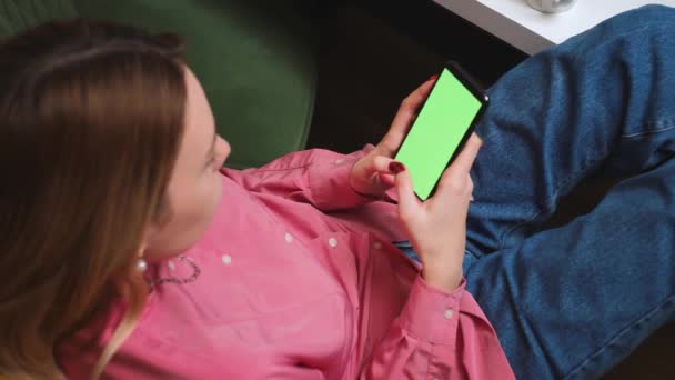 Крупним планом жіночі руки тримають хроматичний зелений екран смартфона, спостерігаючи за вмістом, пропускаючи прокрутку, пише по телефону вдома. Гаджети концепція людей . — стокове відео