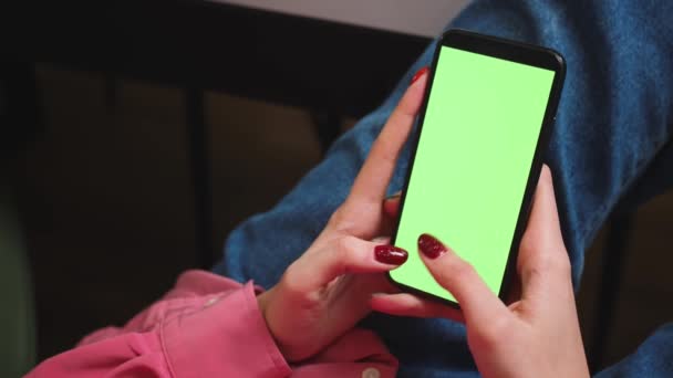 Cierra las manos de mujer sosteniendo el teléfono inteligente de pantalla verde cromakey viendo contenido, deslizando desplazamiento, escribe en el teléfono en casa. Gadgets concepto de personas. — Vídeo de stock