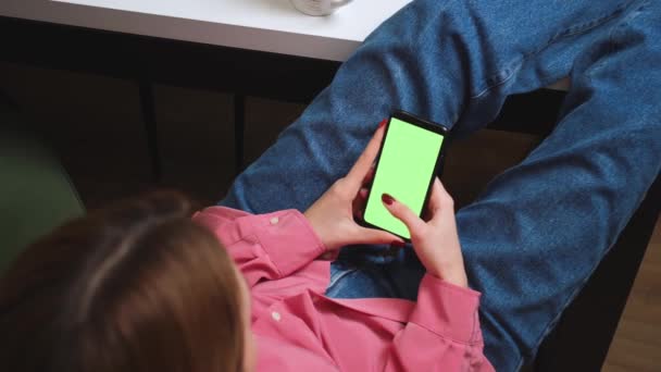 Cierra las manos de mujer sosteniendo el teléfono inteligente de pantalla verde cromakey viendo contenido, deslizando desplazamiento, escribe en el teléfono en casa. Gadgets concepto de personas. — Vídeo de stock