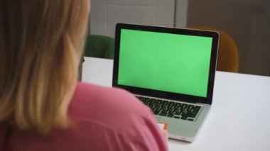 Yeşil ekran dizüstü bilgisayar konsepti: online uzaklık eğitimi, video konferansı. Ev çalışmasında omuz üstü çalışan bayan öğrenci bir not defterine bilgi yazar..