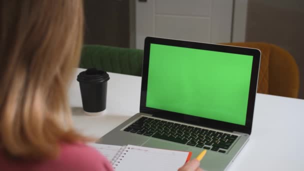 Concetto di computer portatile con schermo verde: istruzione a distanza online, videoconferenza. Sopra la spalla studente donna a casa di studio scrive informazioni in un quaderno. — Video Stock