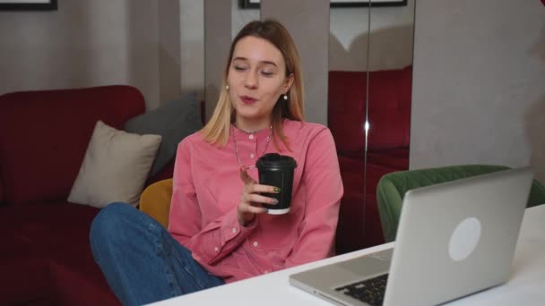 Усміхнена молода жінка сидить вдома з чашкою кави, використовуючи ноутбук, має відео балачки, щаслива жінка спілкується на ноутбуці з другом . — стокове відео