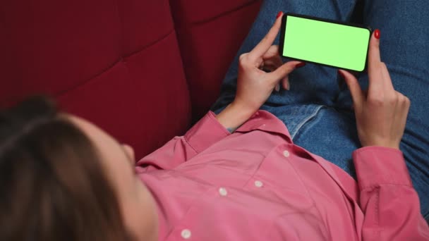 Κοντινό πλάνο χέρια γυναίκα κρατώντας chromakey πράσινο οθόνη smartphone βλέποντας περιεχόμενο, swipping κύλιση στον καναπέ στο σπίτι. Έννοια ανθρώπων gadgets. — Αρχείο Βίντεο
