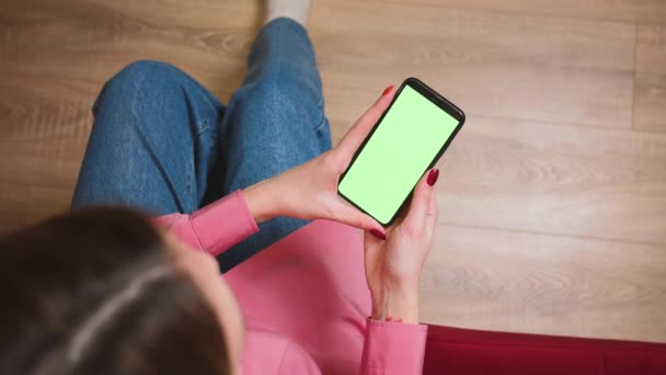 Cierra las manos de mujer sosteniendo el teléfono inteligente de pantalla verde cromakey viendo contenido, deslizando desplazamiento en la oficina en casa. Gadgets concepto de personas. — Vídeo de stock