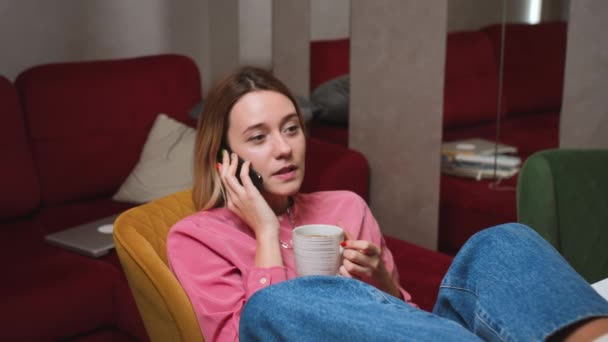 Розслаблена жінка розмовляє мобільним телефоном вдома у повільному русі. усміхнена дівчина говорить смартфон на дивані вдома . — стокове відео