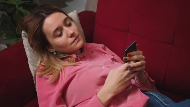 Relaxed Attractive young woman uses phone for online shopping in social media on sofa at home, mobile message communication slow motion — Stock Video