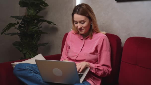 Gelukkig glimlachende blanke vrouw zittend op de bank thuis gebruik en werken aan laptop computer. Vrouwelijke freelancer. — Stockvideo