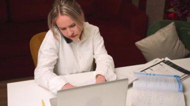 Güzel, genç bir iş kadını telefonda konuşuyor, bilgisayarını kullanıyor, ofis masasında oturuyor, mutlu bir kadın dizüstü bilgisayarla çalışıyor, ev ofisini arıyor..