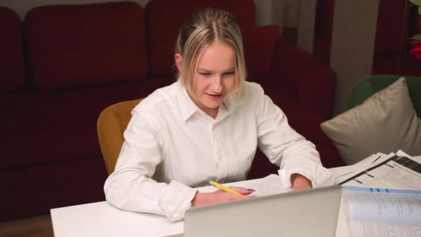 Vrouw met laptop, online afstandsonderwijs, videoconferentie. Vrouwelijke student thuis studie schrijft informatie in een notebook. — Stockvideo