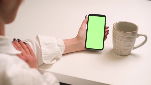 Закрытая женщина держит телефон с зеленым экраном хромакея, девушка смотрит контент, не прикасаясь к экрану гаджета, у женщины есть видеозвонок. Современные технологии и информационная концепция. — стоковое видео