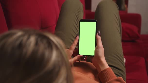 In Großaufnahme halten Frauenhände ein Smartphone mit grünem Chromakey-Bildschirm, das Inhalte anschaut, und wischen auf dem heimischen Sofa herum. Gadgets Menschen Konzept. — Stockvideo