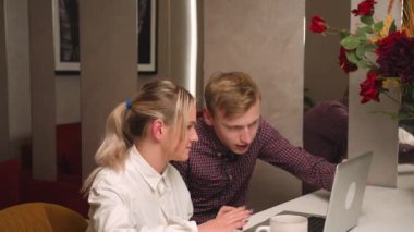 Genç bir çift dizüstü bilgisayar kullanıyor ve çalışıyor, duygusal olarak tartışıyorlar, birlikte online alışveriş yapıyorlar, duygusal olarak gülümseyen bir adam ve evde dizüstü bilgisayarına bakan beyaz bir kadın..