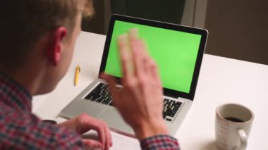 Arka planda el sallayan adam kameranın yeşil ekran kromatonuna el sallıyor. Adamın bilgisayarında kromakey ekranı ile sohbet eden bir video var. Yeşil Ekran. 