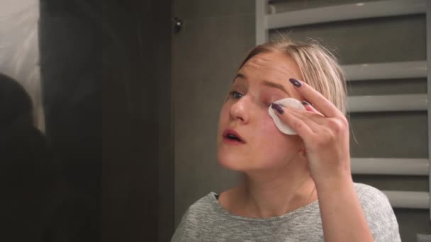 女の子は眉で絵の具を洗う。浴室の女性は鏡を見、綿のパッドと彼女の顔から化粧を拭く。美容師、家庭で化粧だけの概念。閉鎖 — ストック動画