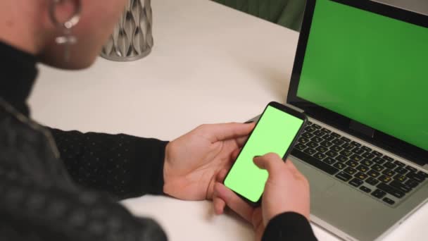 Visszanézni. Zárja be a homoszexuális férfi manikűr használja laptop zöld képernyőn tartja telefon chromakey az otthoni irodában. Tekergetés, koppintás. Férfi néz tartalmat telefon zöld képernyő chromakey. — Stock videók