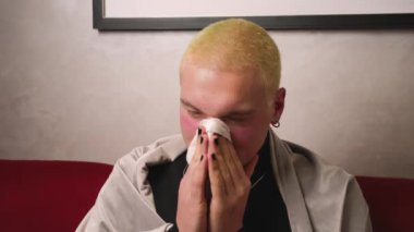 Portredeki homoseksüel adamın kendini battaniyeye saran bir burnu var. Evdeki kanepede oturan sağlıksız bir adam. Hastalık kavramı.