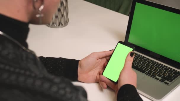 Bakåt. Närbild homosexuell man med manikyr använda laptop grön skärm hålla telefon chromakey på hemmakontoret. Svep rullning, knacka. Man tittar på innehåll på telefon grön skärm chromakey. — Stockvideo