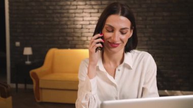 Evde ya da ofiste dizüstü bilgisayarla konuşan güzel, beyaz bir kadın. Masada oturan mutlu iş kadını evde dizüstü bilgisayarla çalışıyor..