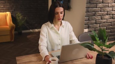 Ev ofisinde dizüstü bilgisayarla çalışan beyaz bir kadın. Masaüstüne yüzüstü düşüyor. İşyerinde bir kadın yanmış..