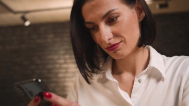 - Yakın çekim. Güzel gülümseyen beyaz kadın telefon kullanıyor, iletişim kuruyor, göz gezdiriyor, içeriği izliyor, evde ya da ofiste sosyal ağlar kuruyor..