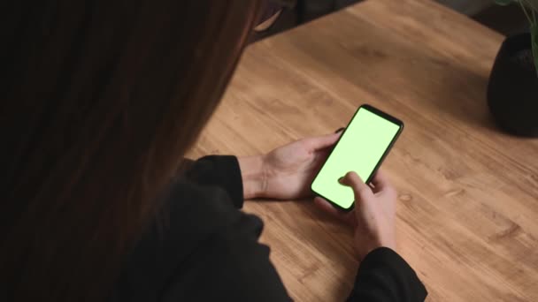 Primer plano. Vista posterior de la mujer sosteniendo la pantalla verde cromakey teléfono inteligente viendo el contenido, deslizando desplazamiento en casa u oficina. Gadgets concepto de personas. — Vídeo de stock