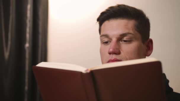 Primo piano. Ritratto di bel giovane che legge un libro, l'uomo ha rilassato il tempo in vacanza a casa. — Video Stock