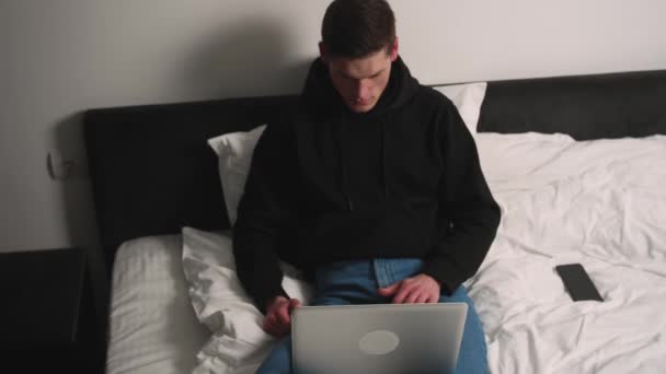 Κουρασμένος όμορφος καυκάσιος άντρας χρησιμοποιεί λάπτοπ στο κρεβάτι αργά το βράδυ πριν κοιμηθεί. Χαμογελώντας άνθρωπος τέλος εργασίας σε φορητό υπολογιστή. — Αρχείο Βίντεο