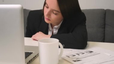 Ev ofisinde dizüstü bilgisayarla çalışan yorgun genç bir kadın. Masaüstüne yüzüstü düşüyor. İşyerinde bir kadın yanmış..