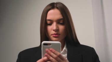 Kapatın. Sosyal medyada online alışveriş için telefonu kullanan, telefona bakan, içeriği izleyen, telefonda yazan ve evdeki ya da ofisteki koltukta oturan çekici genç kadının portresi.